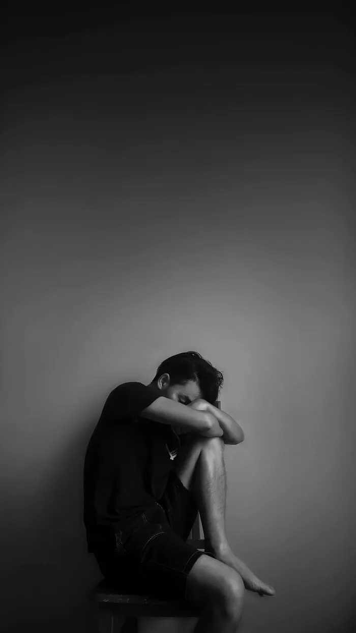 Person sitting with head on knees, symbolizing overlooked traumatizing experiences in a dimly lit room.