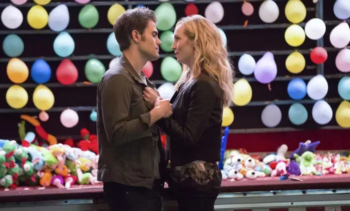 A TV couple holding hands at a carnival game, surrounded by balloons, lacking chemistry.