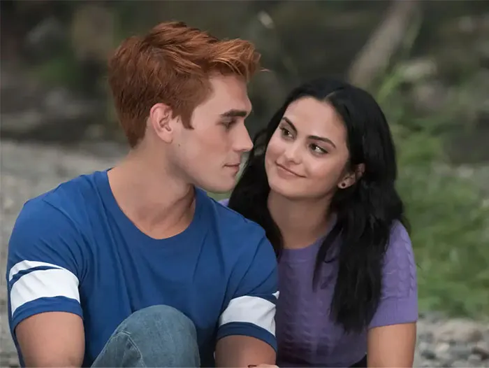 TV couple with little chemistry, sitting outdoors, girl smiling at boy in a blue shirt.
