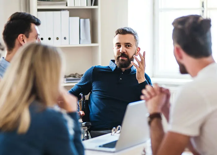 A man in a team meeting, discussing workplace issues with colleagues around a table.