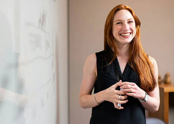Smiling woman in a black top standing by a whiteboard, representing a positive workplace environment.