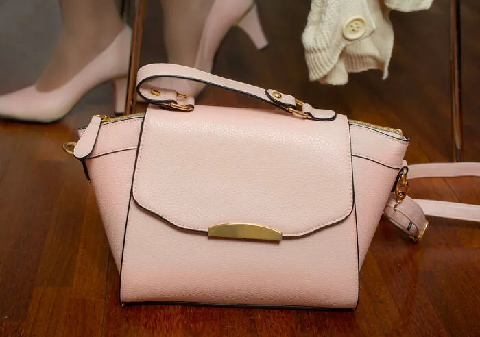 A pink handbag on a wooden floor, related to superstitions about placing bags on the ground.