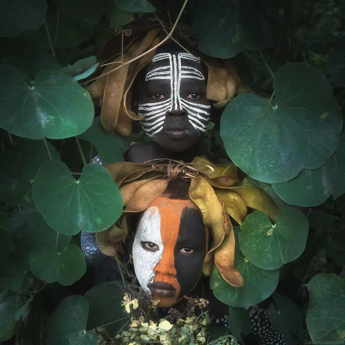 Ethiopian people with traditional face paint, surrounded by lush greenery in Daniel Kordan's captivating photograph.