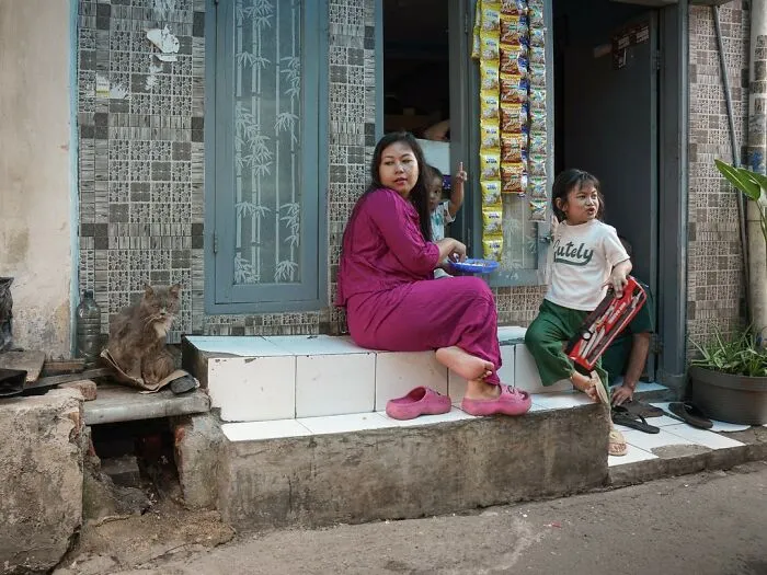 Woman and child sit on steps next to a cat in a city scene, captured by Marcel Heijnen.