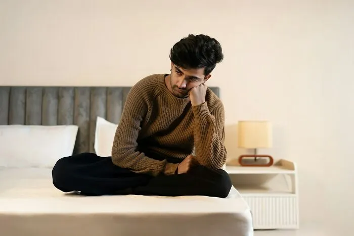 A person sitting thoughtfully on a bed, reflecting on financial decisions and life lessons.
