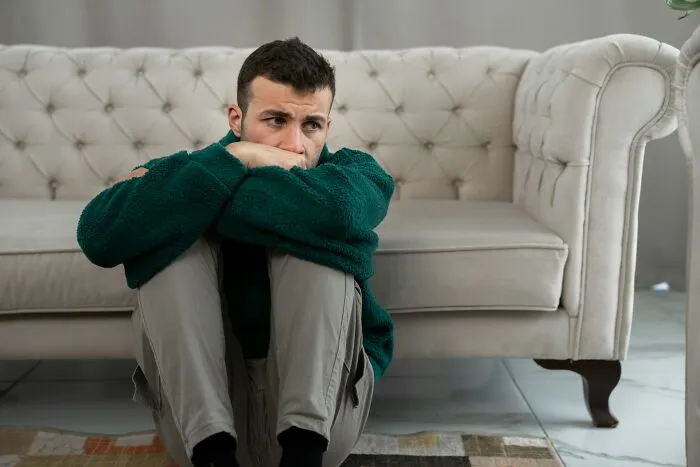 Man sitting on the floor, looking thoughtful, possibly reflecting on financial decisions and life lessons.