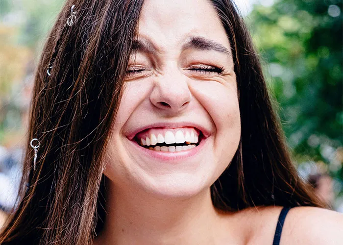 Mujer joven sonriendo con ojos cerrados mostrando rasgos poco atractivos que resultan encantadores y atractivos.