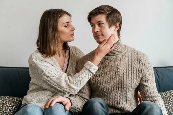 A couple sitting on a sofa, a woman gently touches a man's face, illustrating expressions of love and affection.