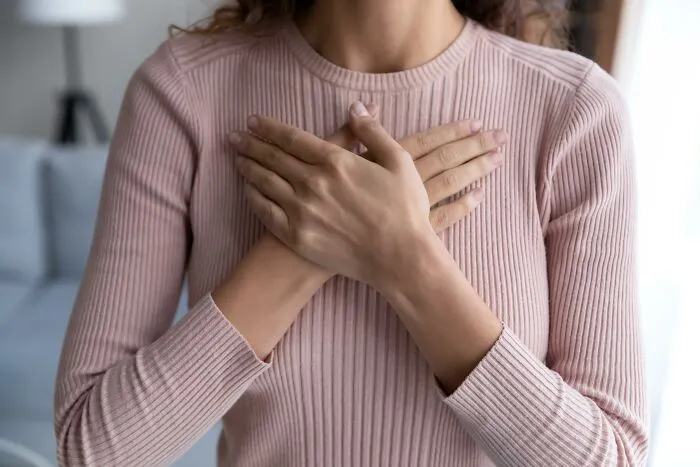 Person in a pink sweater with hands on chest, expressing love and care.