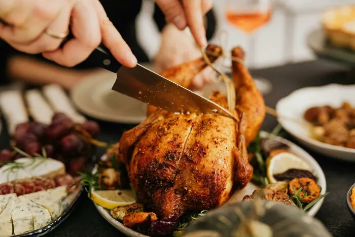 Carving a roast chicken on a dining table with accompanying sides; evokes a warm, festive setting.