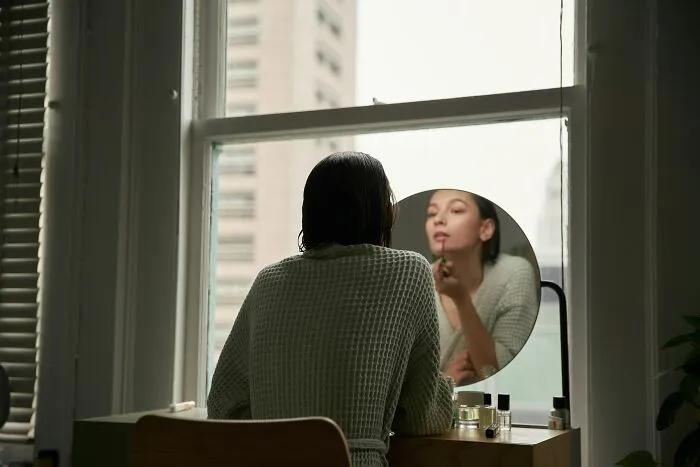 Person applying makeup in front of a window, representing life improvement habits.