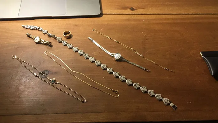 Gold jewelry and watches found while dumpster diving displayed on a wooden table.