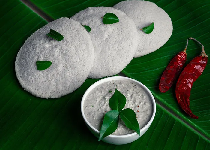 Idli with chutney and chillies on banana leaves, showcasing foods people love as they grow up.