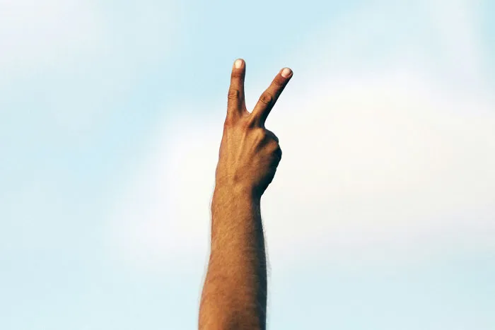 Hand making a peace sign against a blue sky, suggesting funny email sign-offs.