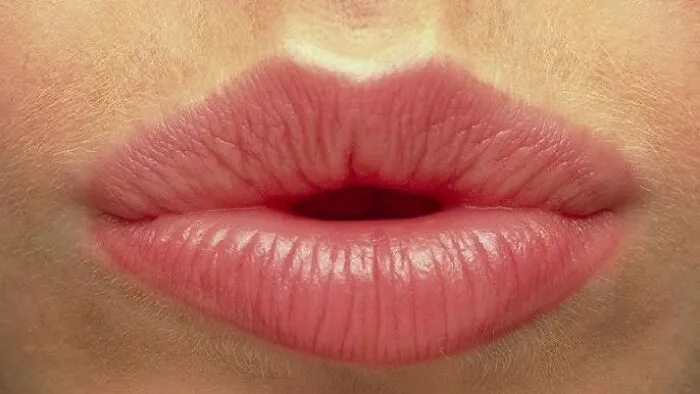 Close-up of lips forming a whistling shape, related to superstitions about whistling indoors on a dark background.