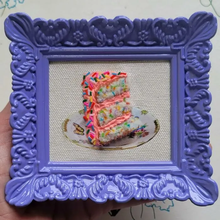 Hyper-realistic embroidered dessert of a colorful layered cake framed in a decorative, ornate purple frame.