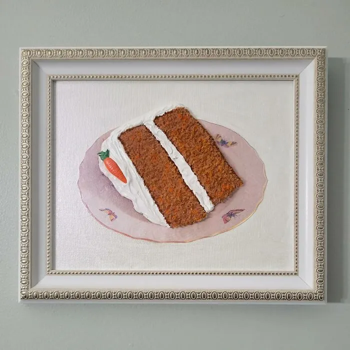 Hyper-realistic embroidered dessert of a carrot cake slice in an ornate frame on a wall.