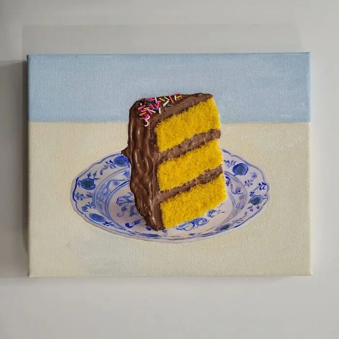 Hyper-realistic embroidered cake slice with yellow layers, chocolate icing on a blue patterned plate.