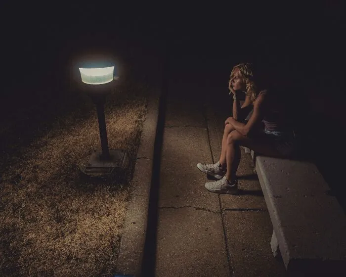 Person sitting alone on a bench at night, illuminated by a streetlamp, representing underrecognized traumatizing experiences.