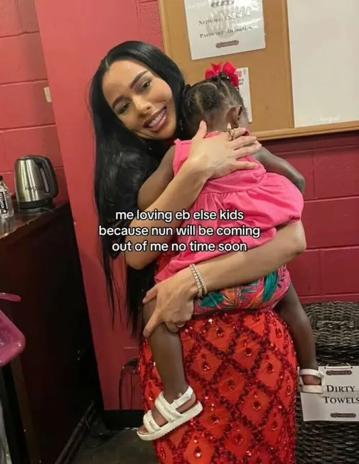 Woman in a red skirt holding a child, smiling, with humorous text about kids as a "Just Girly Things" meme.