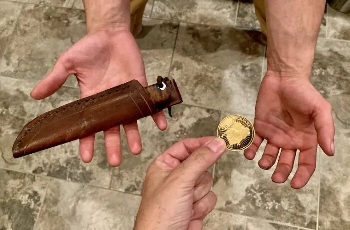 Hands exchanging a sheathed knife and a coin, illustrating superstitions about gifting knives.