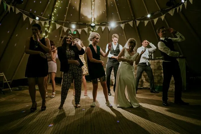 Wedding guests dancing under string lights inside a decorated tent.