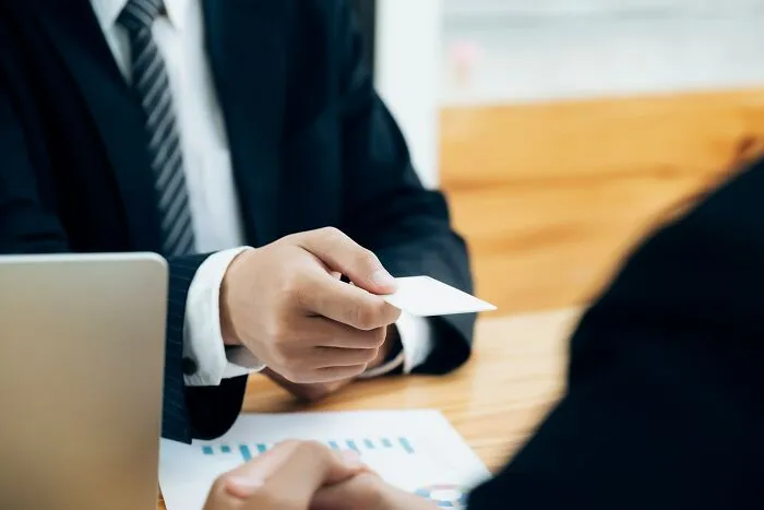 A person in a suit handing a business card across a table, illustrating sentimental reasons for carrying items.