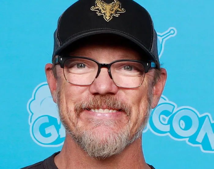 Man with glasses and a cap smiling at a comic event.