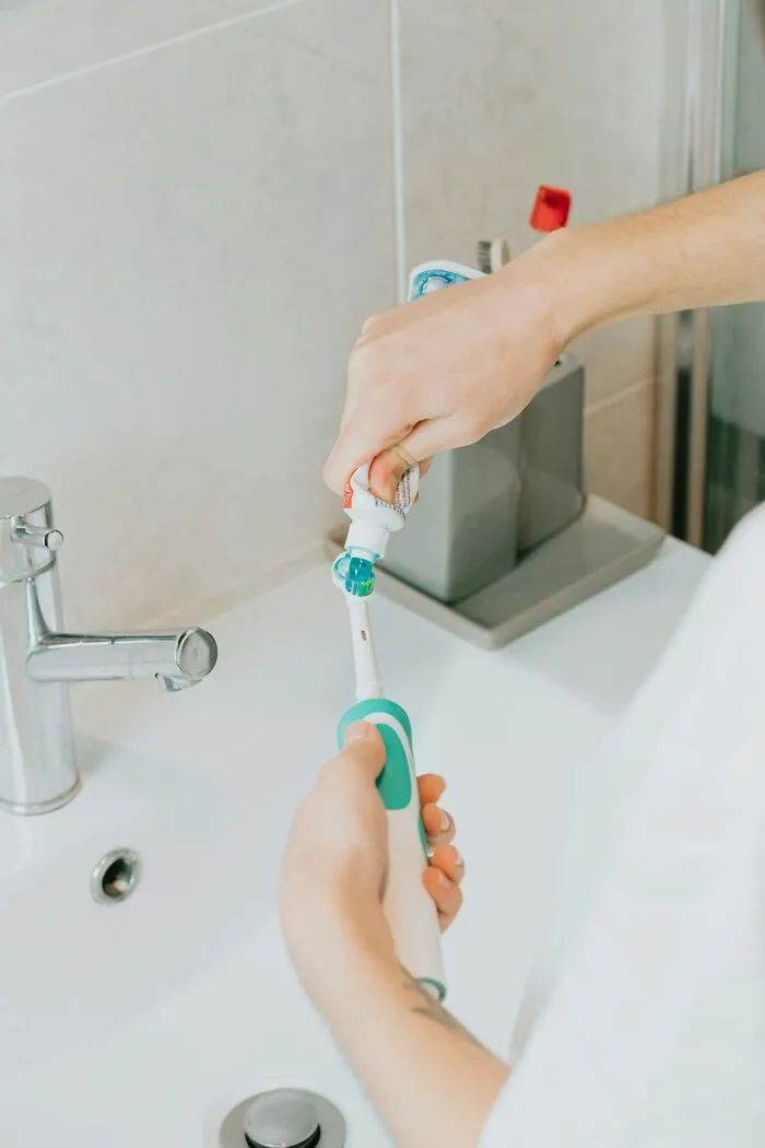 Person applying toothpaste to an electric toothbrush, part of a thread on life improvements.