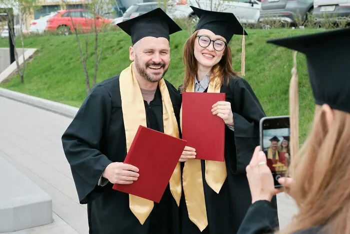Graduates in caps and gowns smiling with diplomas, capturing a life-improving moment being photographed outdoors.