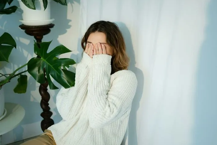 Person in a cozy sweater sitting beside plants, face partially covered, reflecting on life improvements.
