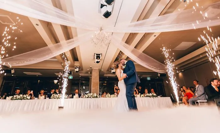 Couple kissing under wedding decorations with guests seated, sparklers around, capturing what wedding guests may dislike.