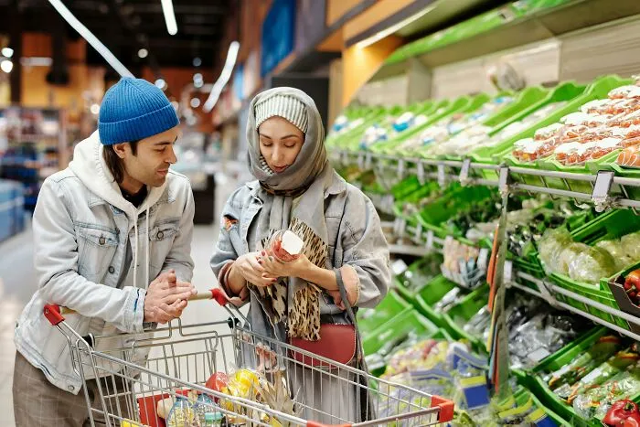 Couple by grocery cart, sharing hilarious overheard conversations while shopping for produce.
