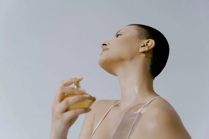 Person applying perfume on neck, illustrating social rules people ignore in grooming routines.