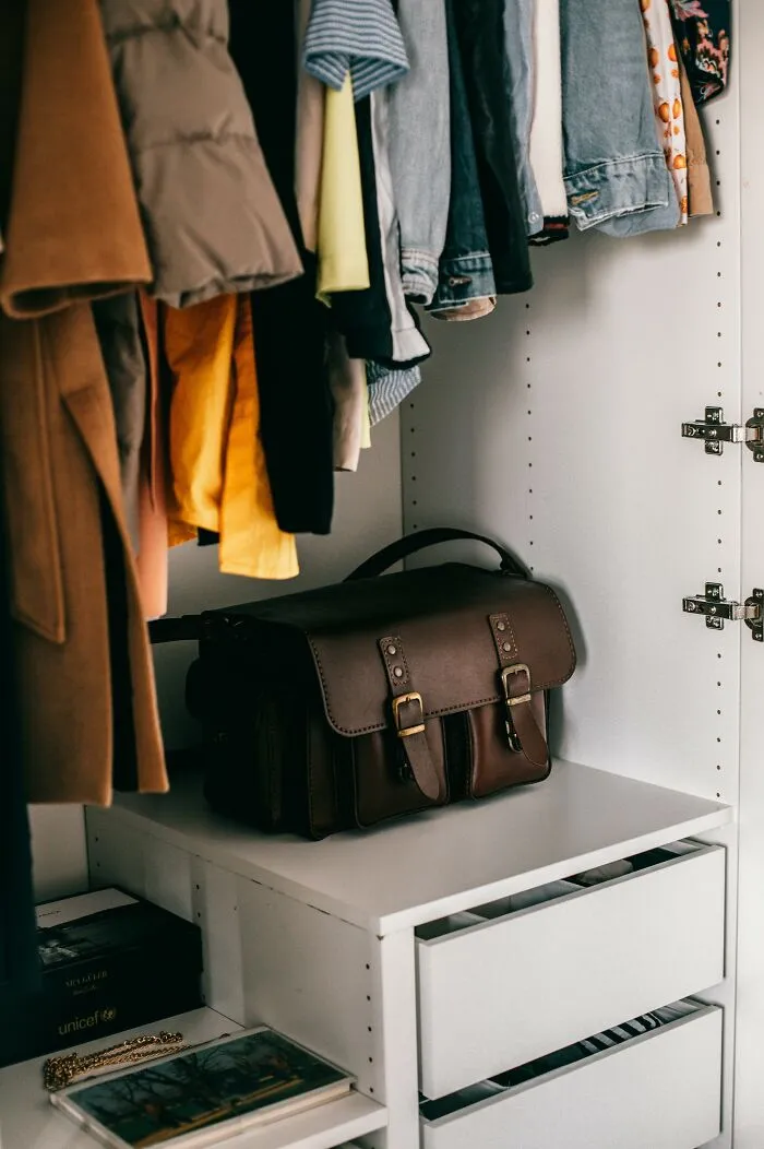 Organized closet with folded clothes and a leather satchel, showcasing life improvement through tidiness.