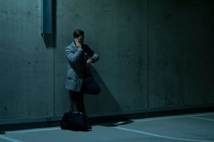 Man in a dark parking garage, talking on phone, checking watch. Keywords: wedding guests.