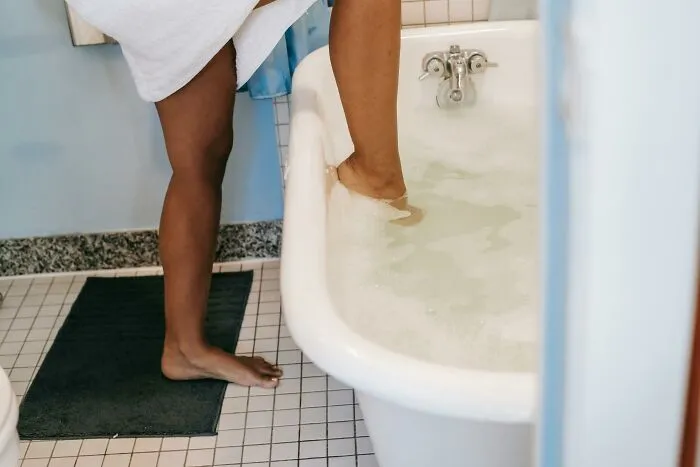 Person stepping into a bathtub with water, wrapped in a towel, capturing a relatable moment for hilarious overheard conversations.