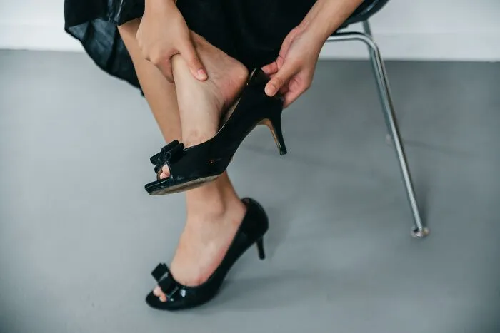 Person removing high heels in discomfort, highlighting social rules people ignore about footwear etiquette.