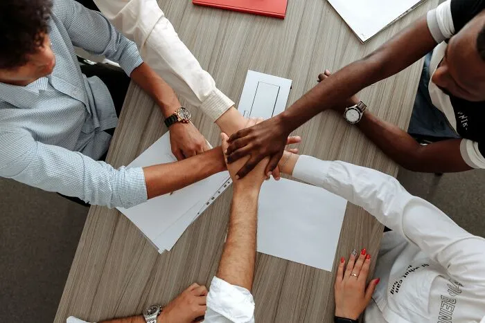 "Hands joined in unity over an office table, symbolizing teamwork and collaboration."