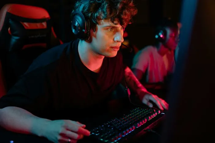 Person gaming on a computer, wearing headphones, possibly listening to hilarious overheard conversations.