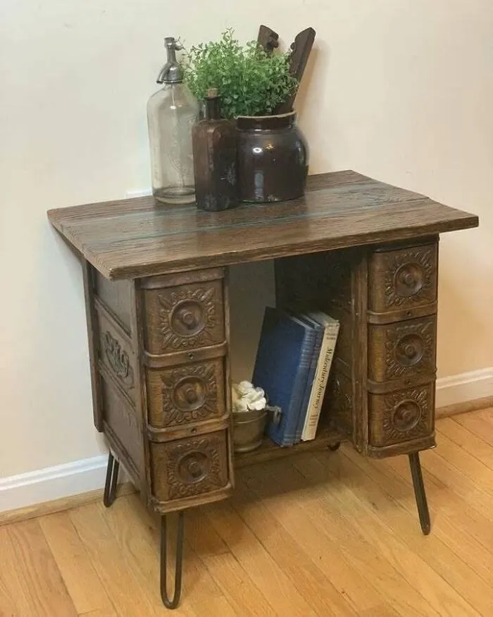 Recycled wooden cabinet with ornate drawers, topped with plants and glass bottles on a wooden floor.