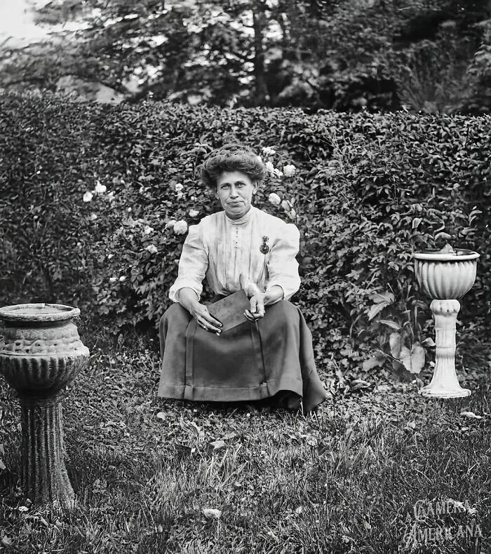 Una mujer se sienta o se pone en cuclillas en su jardín con un libro en la mano, una postura poco convencional para la época, principios del siglo XX