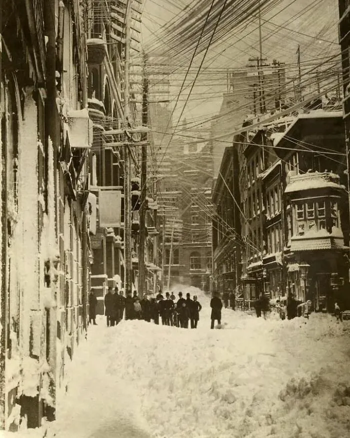 Calle nevada con edificios antiguos y cables enredados, escena histórica evocando días pasados.