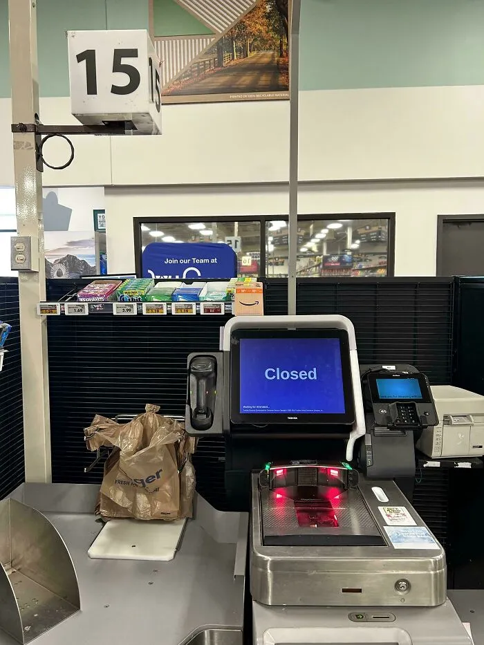 Caja de supermercado autoservicio cerrada con bolsas y productos, empleados frustrados contando historias de clientes difíciles.