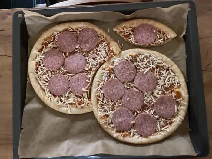 Unusual pizza shapes on a baking tray with salami and cheese, showcasing an unexpected twist on classic pizza.