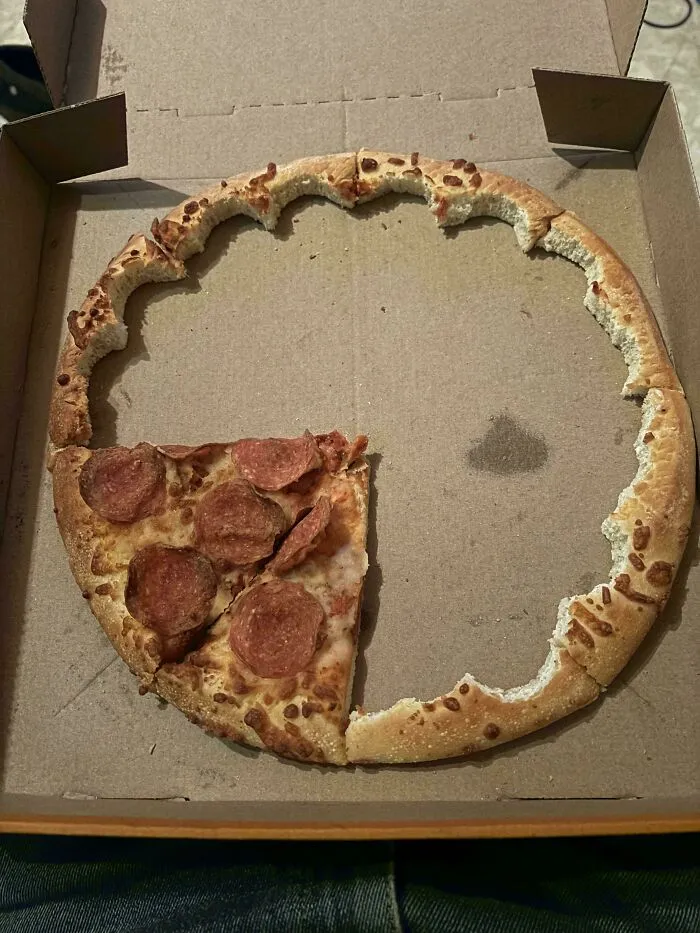 Pepperoni pizza with crust eaten away creating a ring, leaving a single slice in a cardboard box.