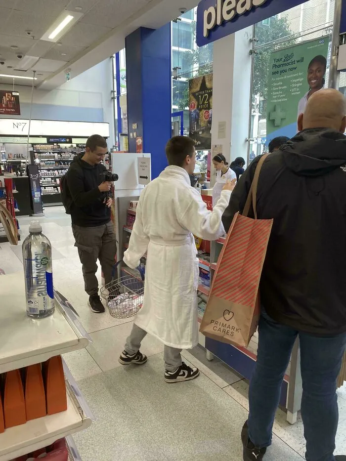 Influencer vestido en bata de baño comprando en una farmacia mientras lo filman.