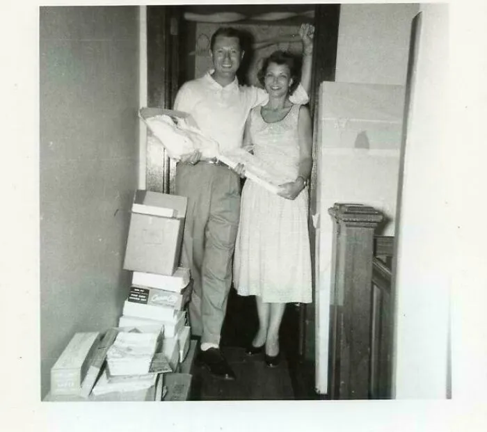 Black and white candid vintage photo of a smiling couple posing inside a hallway with stacked boxes, history glimpse