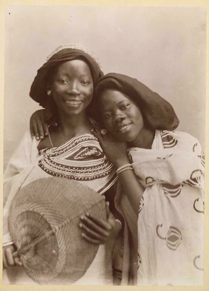 Pareja de mujeres de Zanzíbar, Tanzania, posan para un retrato con sonrisas radiantes, década de 1900.