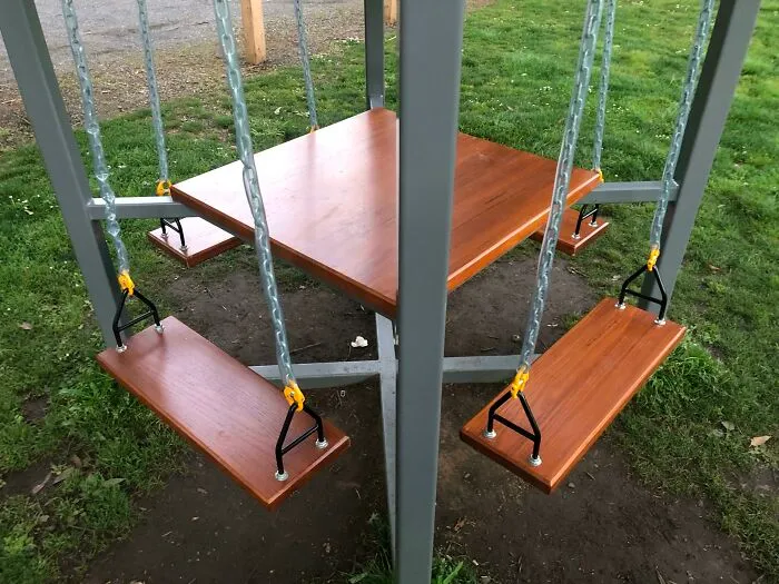 Diseño curioso de columpios y mesa en un parque, que no parece práctico en la realidad.
